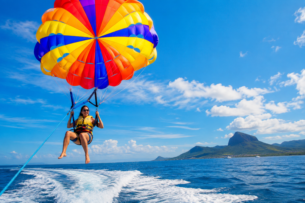 Activité de parasailing à l’Île aux Cerfs à l’île Maurice, avec une personne survolant le lagon turquoise sous un parachute coloré face aux montagnes tropicales